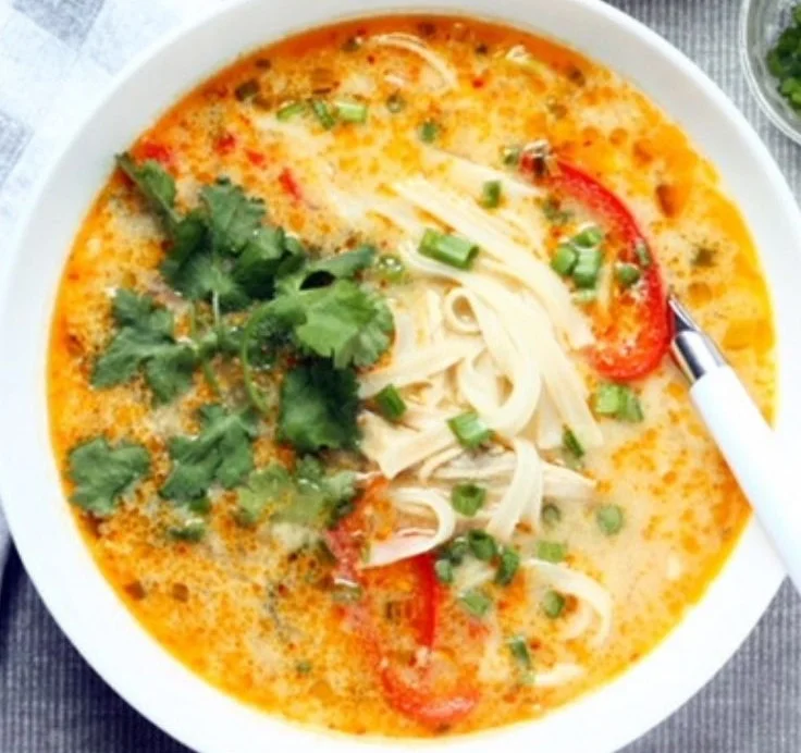 A bowl of 30-minute Thai chicken noodle soup garnished with herbs.