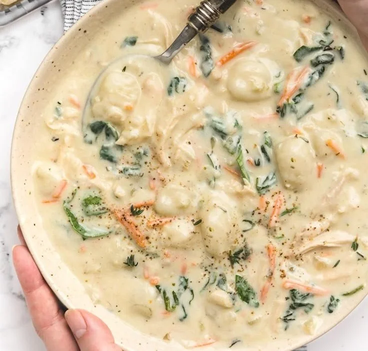 Bowl of creamy chicken gnocchi soup garnished with herbs and vegetables