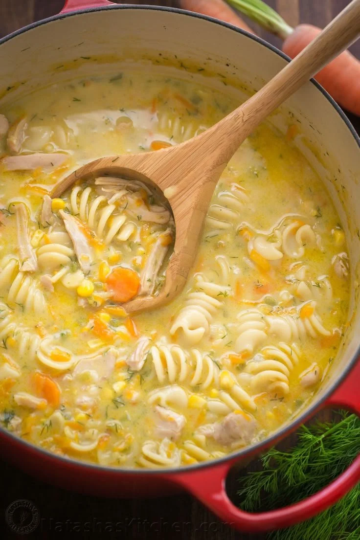 A bowl of creamy chicken noodle soup with vegetables and herbs