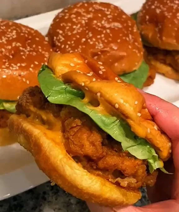 Crispy fried chicken sandwich with toppings and sauce on a wooden plate