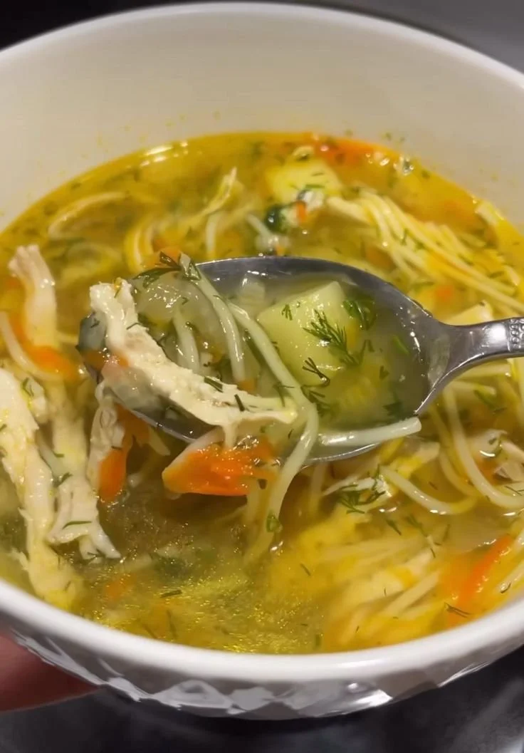 A steaming bowl of homemade chicken noodle soup with fresh ingredients.