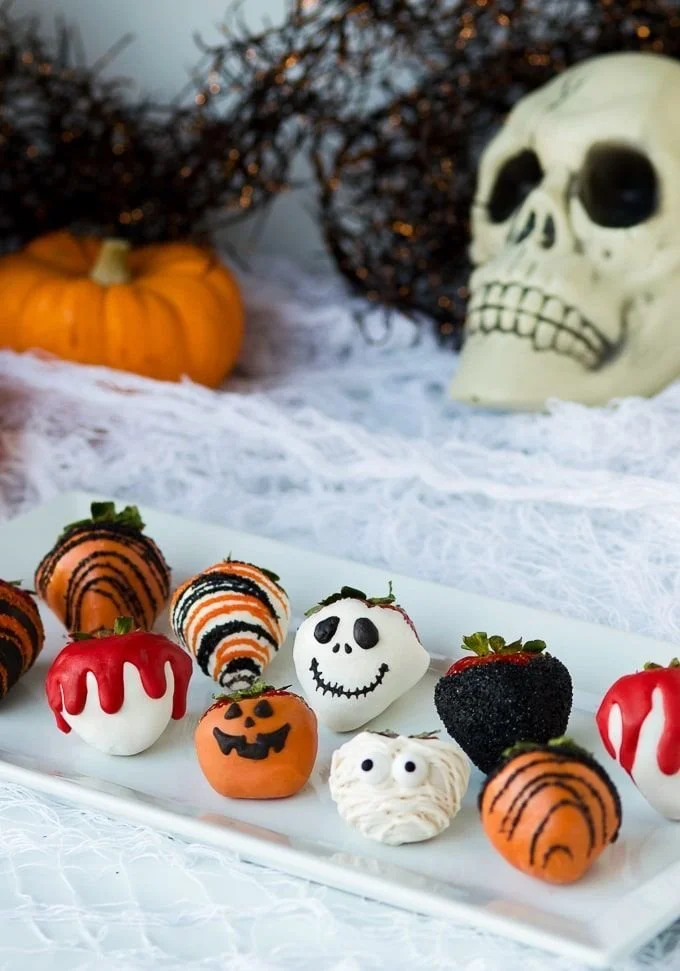 Halloween-themed chocolate covered strawberries decorated with spooky designs.