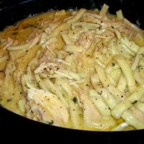 A bowl of savory chicken noodles with vegetables garnished with herbs.